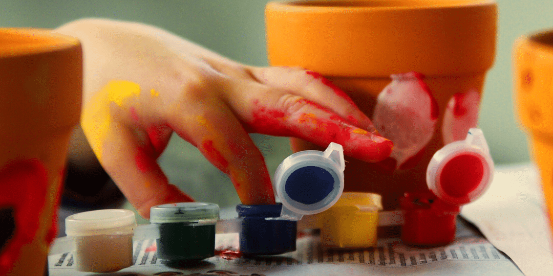 Child using their fingers to paint a terracotta pot