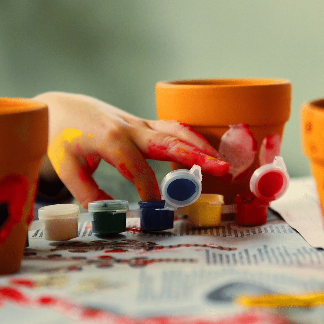 Child using their fingers to paint a terracotta pot